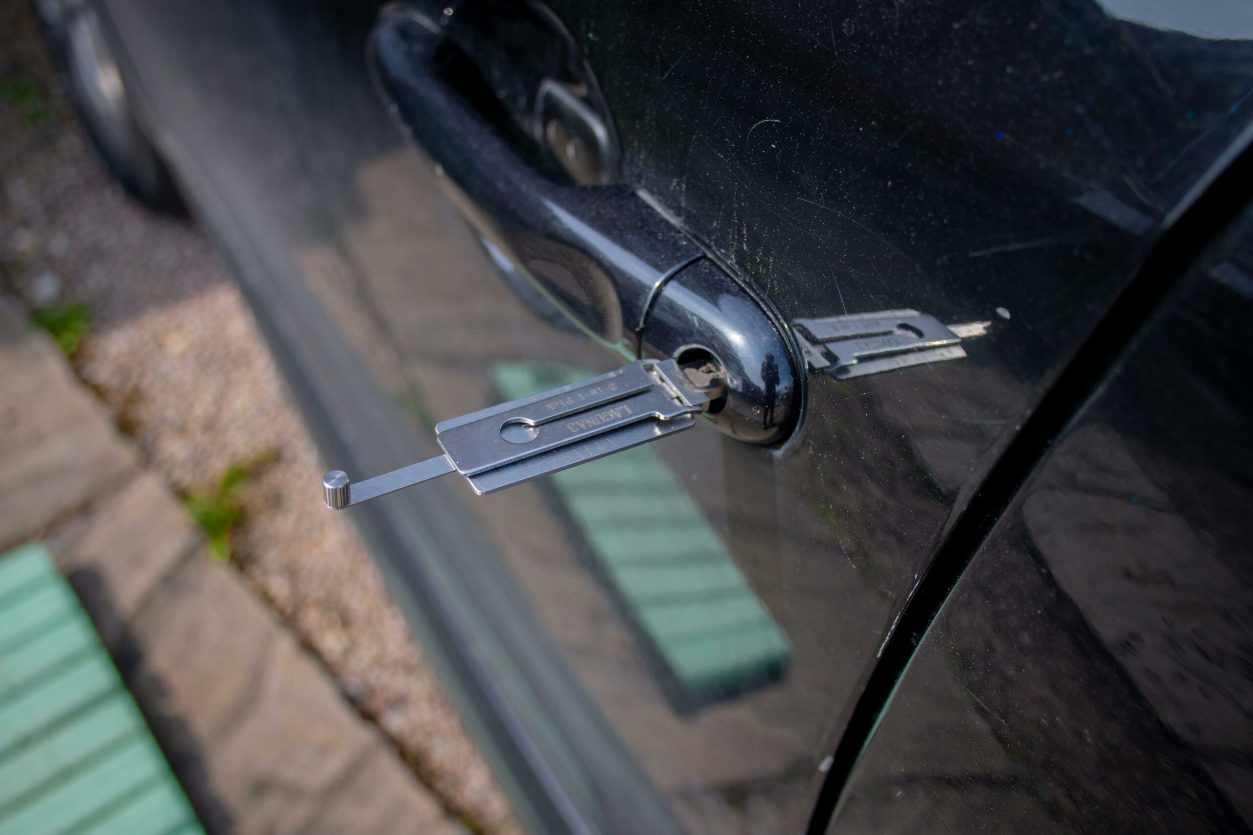 Acceuil Close-up of a locksmith tool inserted into a car door lock, demonstrating security access.