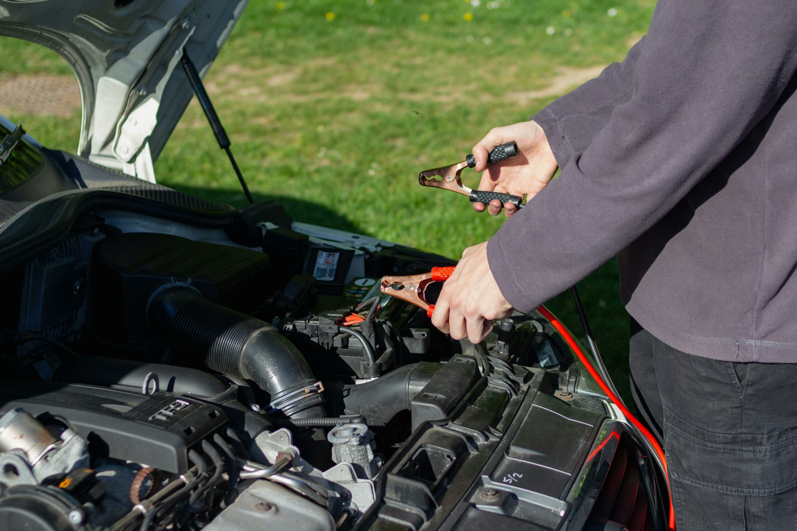 Acceuil Close-up of mechanic using jumper cables to jump-start a car battery outdoors.
