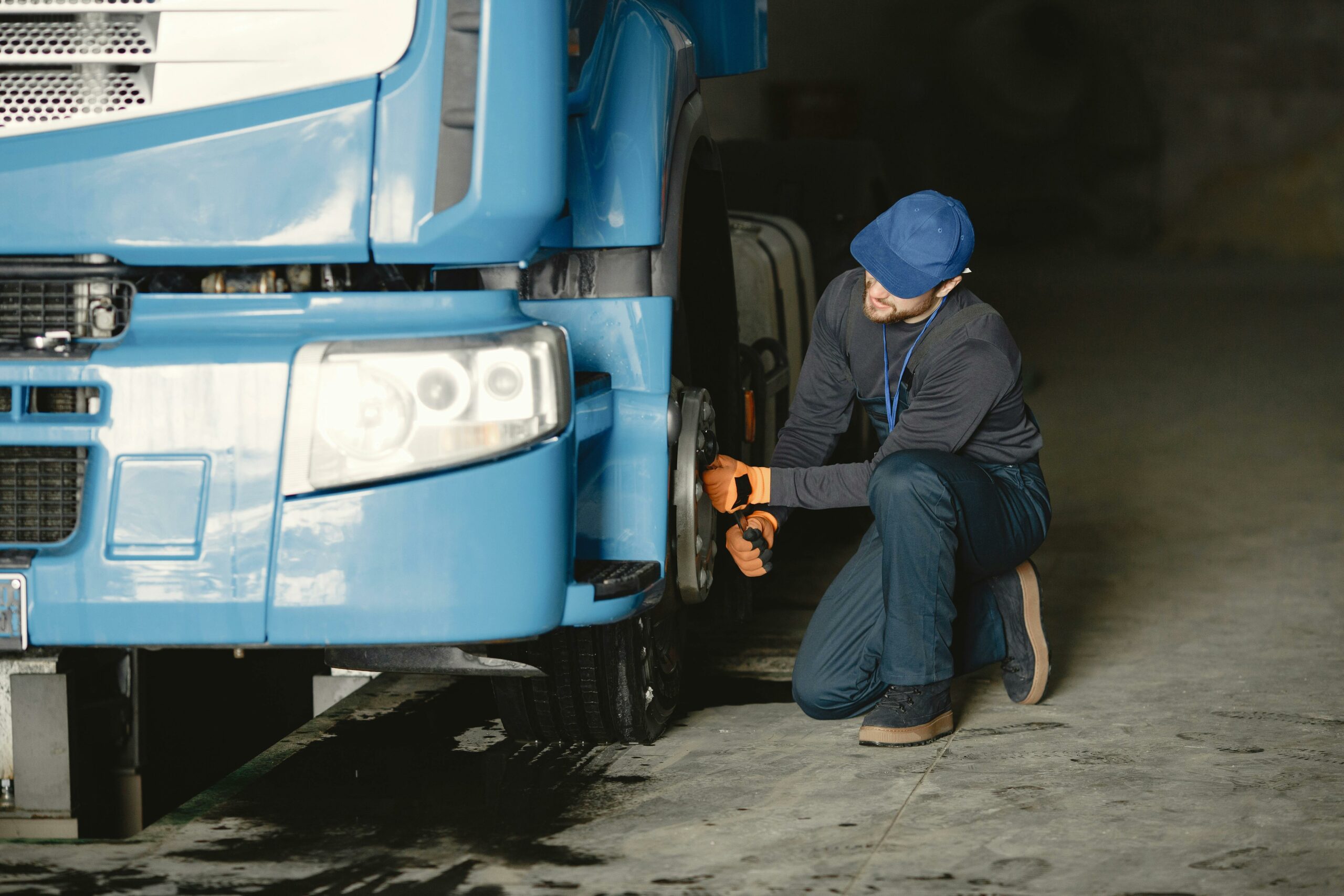 Acceuil Mechanic in a garage fixing the wheel of a blue truck. Industrial vehicle maintenance.